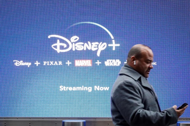 a man looks at his phone as he passes by a screen advertising walt disney 039 s streaming service disney in new york city us november 12 2019 photo reuters