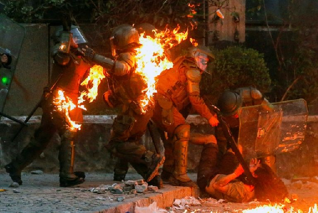 a demonstrator is held while a petrol bomb hits riot police during a protest against the government in santiago photo afp