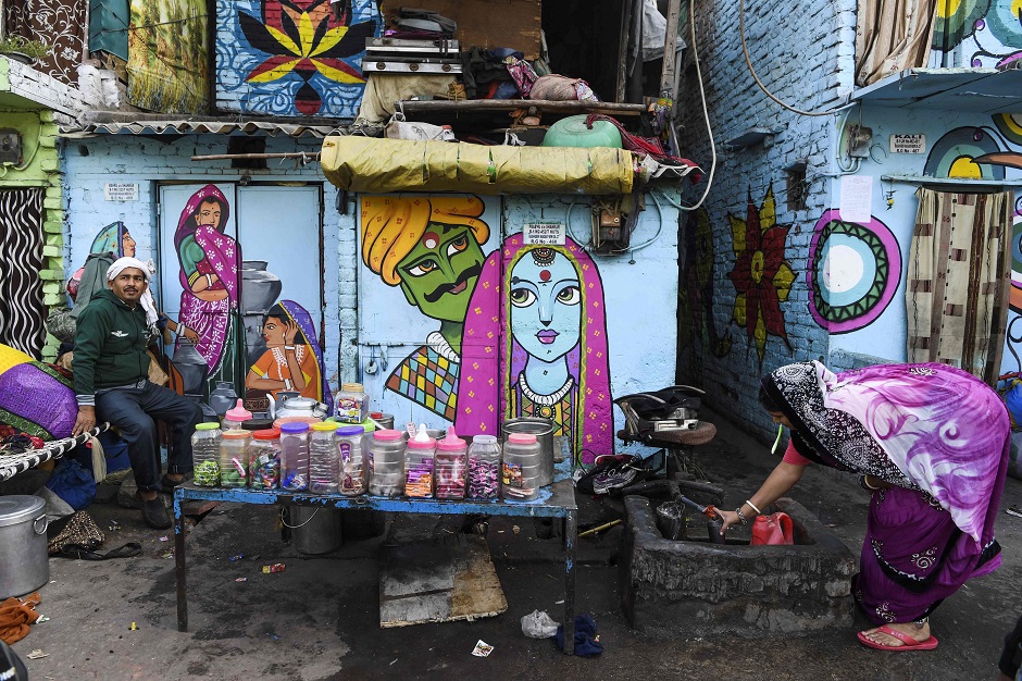 a woman collects water in front of a home adorned with murals painted by artists from 039 delhi street art 039 group at the raghubir nagar slum in new delhi photo afp