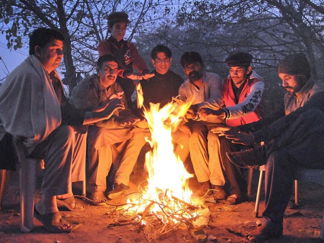 people sit around fire to keep warm in cold weather in islamabad photo app