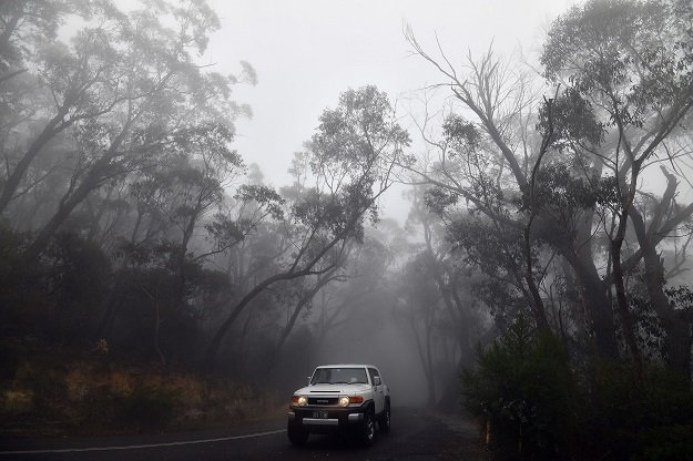 a car makes its way through thick fog mixed with bushfire smoke in the ruined castle area of the blue mountains some 75 kilometres from sydney photo afp