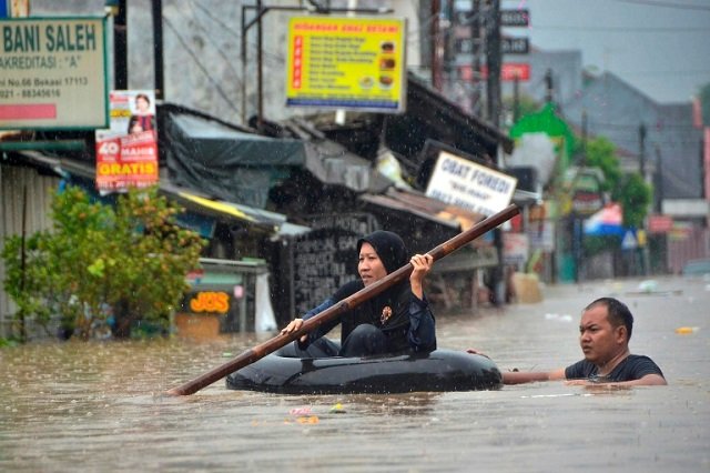 a woman paddles through flood waters on an inner tube in bekasi near jakarta photo afp