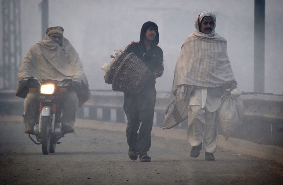 a motorcyclist passes by men walking along a road in dense fog on a cold day in lahore photo reuters