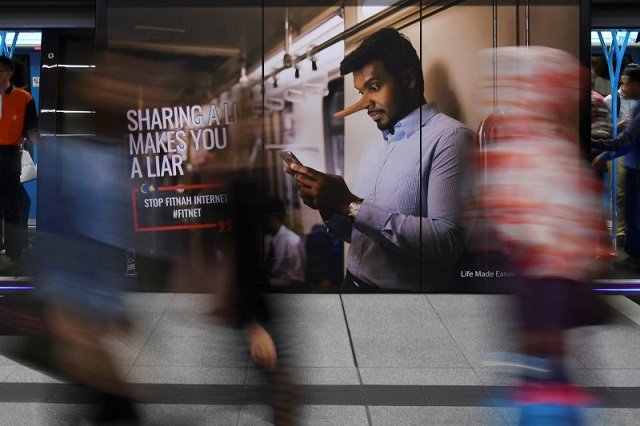 commuters walk past an advertisement discouraging the dissemination of fake news at a train station in kuala lumpur malaysia march 28 2018 photo reuters