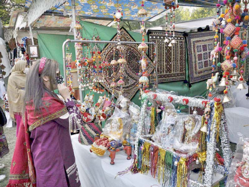 a visitor takes keen interest in cultural and traditional items while an elderly woman weaves clothes on a handloom at a mela photo online file