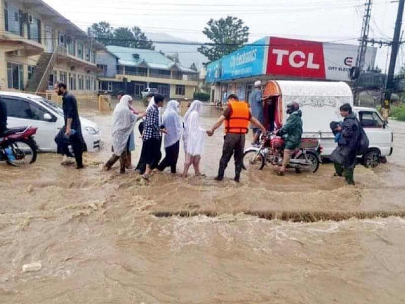 rescue officials help women cross a flooded road in abbottabad photo ppi