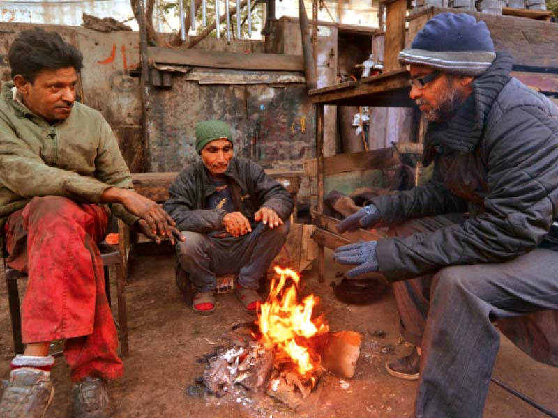 mechanics chat as they sit around a fire during a lean hour at their workshop in a karachi neghbourhood on thursday photo jalal qureshi