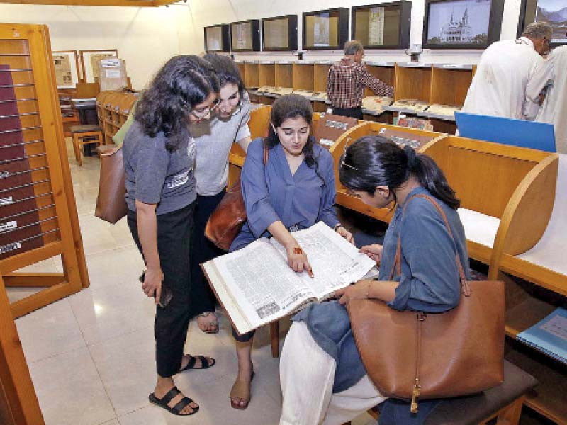 women read an old newspaper at the sindh archives department as part of an exhibition held to mark the international archives day photo ppi