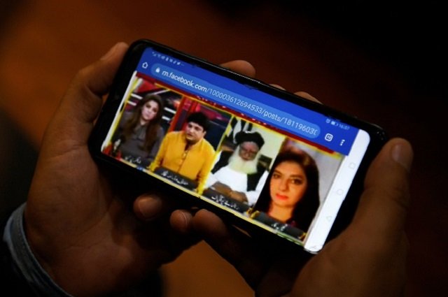 a man watches a video clip on his mobile phone about a debate on aurat march between women rights activist marvi sirmed r and television play writer khalil ur rehman 2l in islamabad photo afp