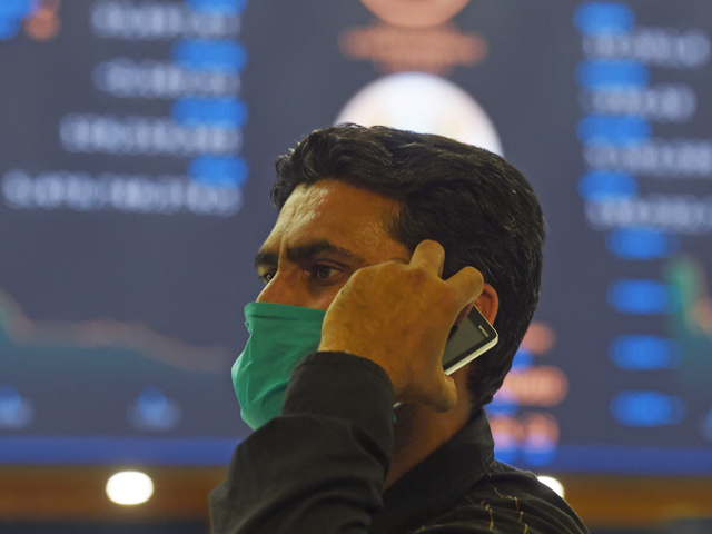 a stockbroker wearing a facemask amid concerns over the spread of the covid 19 novel coronavirus holds a mobile phone during a trading session at the pakistan stock exchange psx in karachi on march 16 2020 photo afp