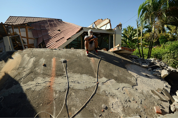 A man sits on the debris at Sigar Penjalin village in northern Lombok. PHOTO:AFP