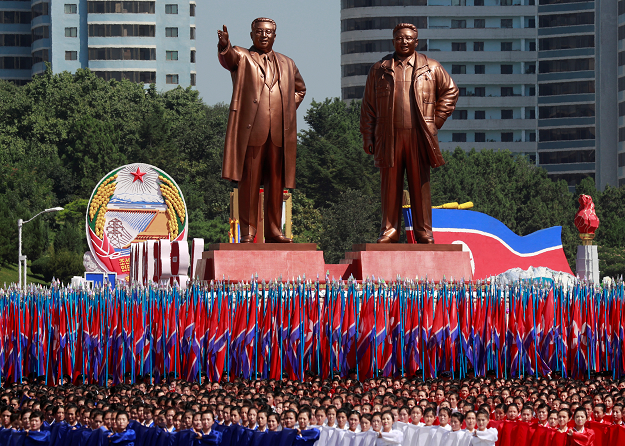  People carry flags in front of statues of North Korea founder Kim Il Sung and late leader Kim Jong Il during a military parade. PHOTO:REUTERS