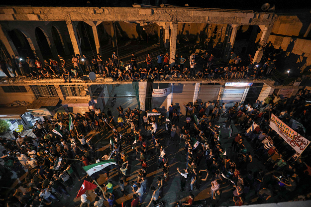 Syrians chant slogans and wave flags of the opposition as others stand on an upper floor of a damaged building during a protest against the Syrian government in Binnish in the rebel-held northern Idlib province. PHOTO: AFP