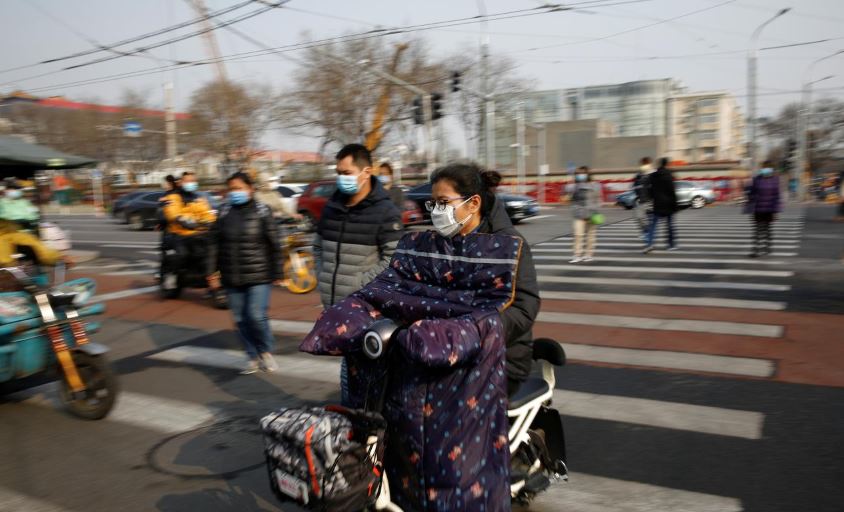 people wearing face masks ride their scooters and walk on a street following an outbreak of the coronavirus disease covid 19 in beijing china march 30 2020 photo reuters