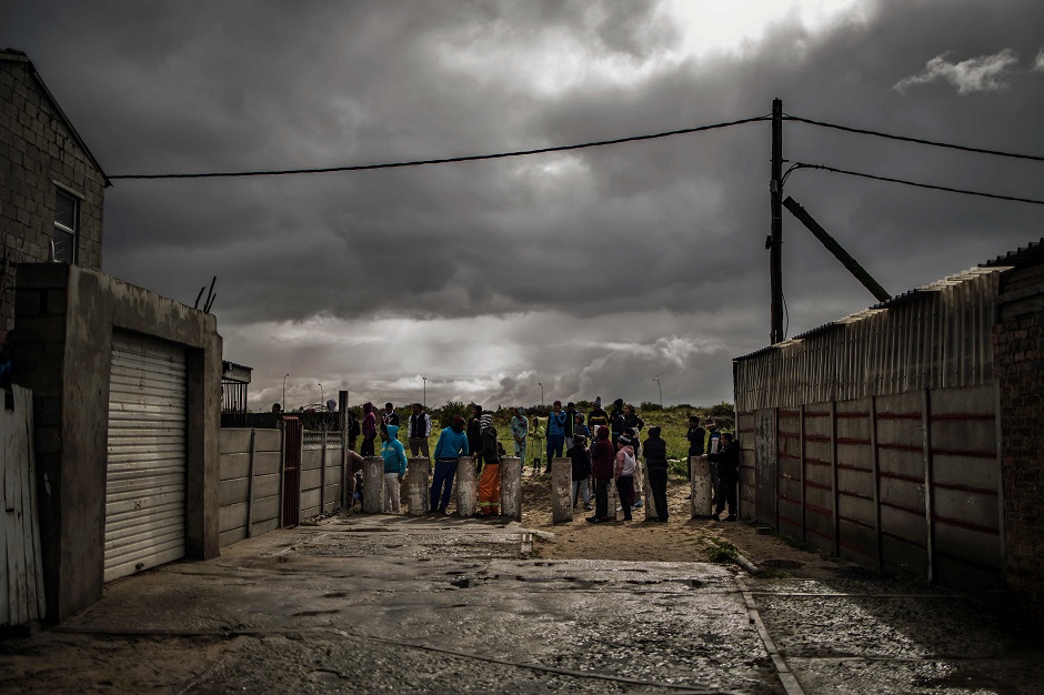 Residents gather to observe the movements of South African anti-riot policemen patroling a street during a police operation for a service delivery protest called by rights organisations in the Cape Flats area in Cape Town. PHOTO: AFP