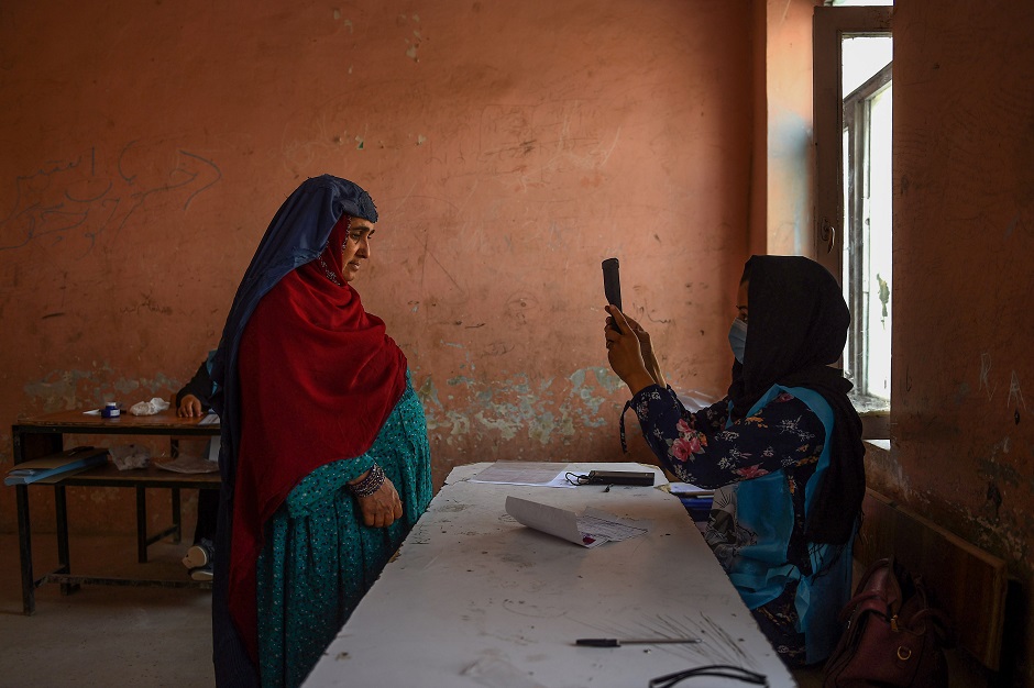 An Independent Election Commission (IEC) official (R) scans a voter's face with a biometric device at a polling station in Mazar-i-Sharif. PHOTO: AFP