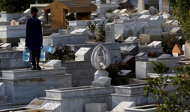 a boy with water filled containers for sale stands on a grave while waiting for people during a lockdown after a government imposed ban on visiting graveyards for shab e barat festival following the spread of coronavirus disease covid 19 in karachi pakistan april reuters