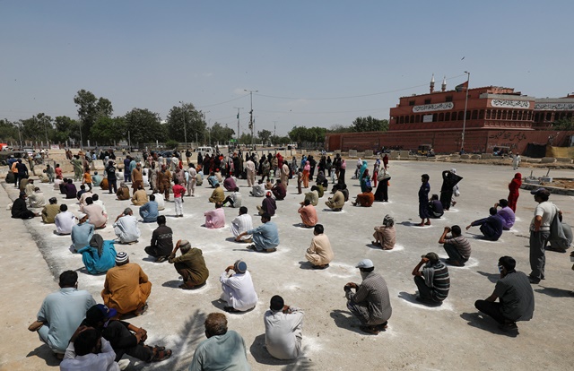 people sit on the ground in circles drawn with chalk to maintain safe distance as they wait to receive sacks of ration handouts from a distribution point of a charity during a partial lockdown after pakistan shut all markets public places and discouraged large gatherings amid an outbreak of coronavirus disease covid 19 in karachi pakistan march 29 2020 reuters akhtar soomro