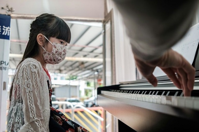 six year old hong kong student yoyo wears a facemask during a piano lesson in the back of a truck with teacher evan kam photo afp