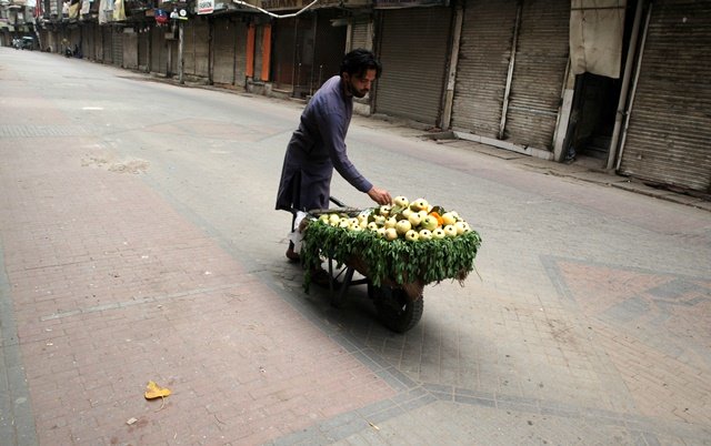 a fruit vendor waits for customers as he sells guava from a wheelbarrow along a closed market during a lockdown following an outbreak of coronavirus disease covid 19 in lahore pakistan march 31 2020 reuters mohsin raza