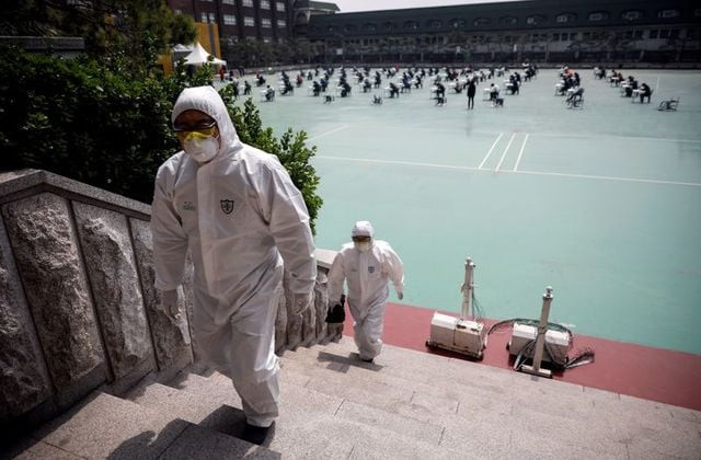 people in personal protective equipment walk up a flight of stairs as south korean job seekers background attend an exam conducted outdoors amid social distancing measures to avoid the spread of the coronavirus disease covid 19 in seoul south korea april 25 2020 photo reuters