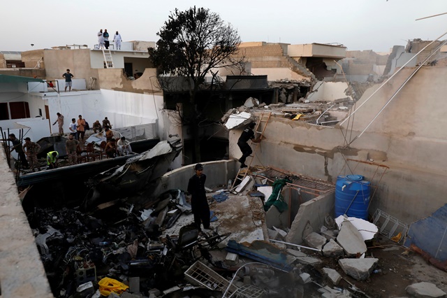 people stand on a roof of a house amidst debris of a passenger plane crashed in a residential area near an airport in karachi pakistan may 22 2020 reuters