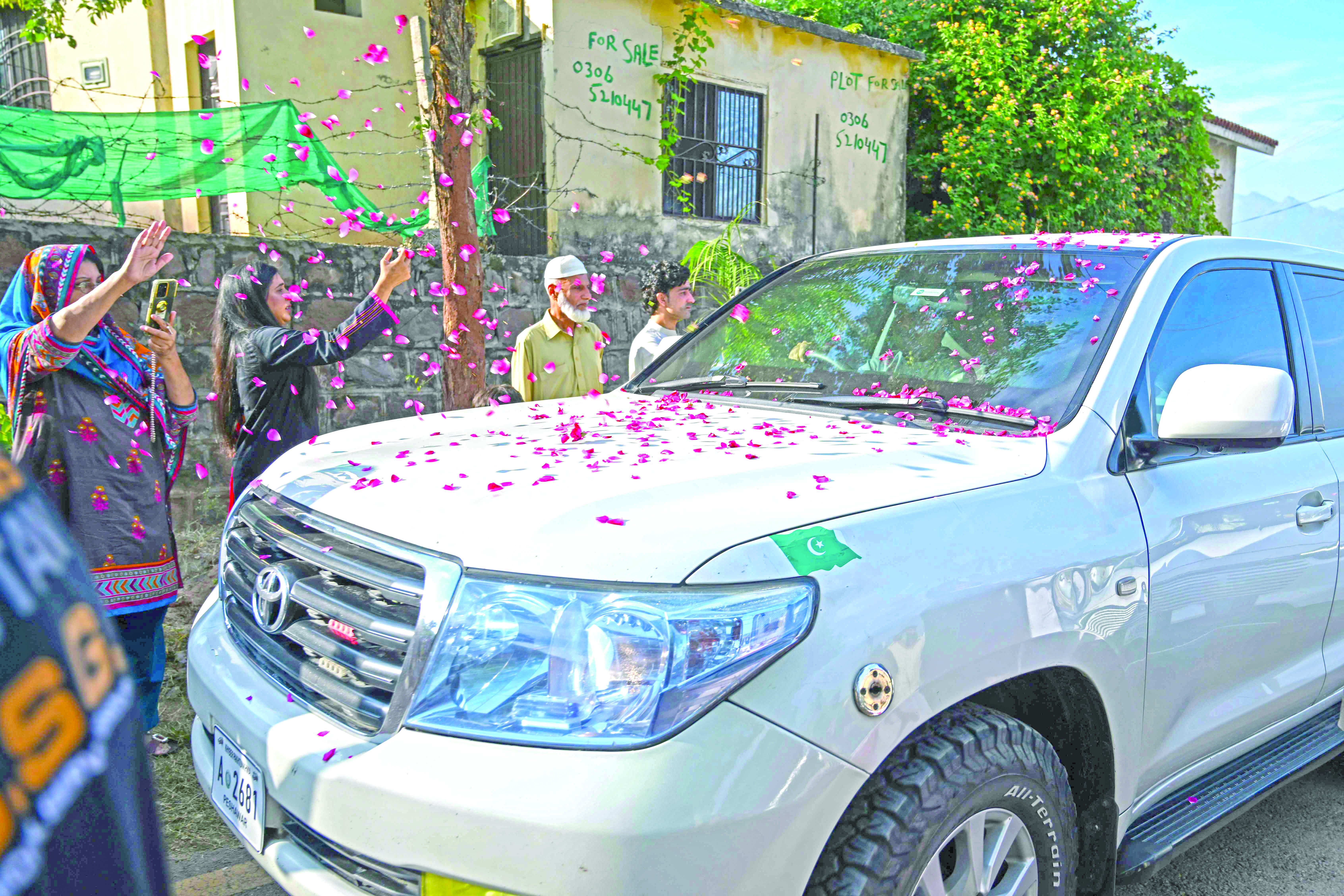 supporters shower rose petals on a car carrying bushra bibi the wife of pti founder imran khan as she arrives in bani gala in islamabad photo afp