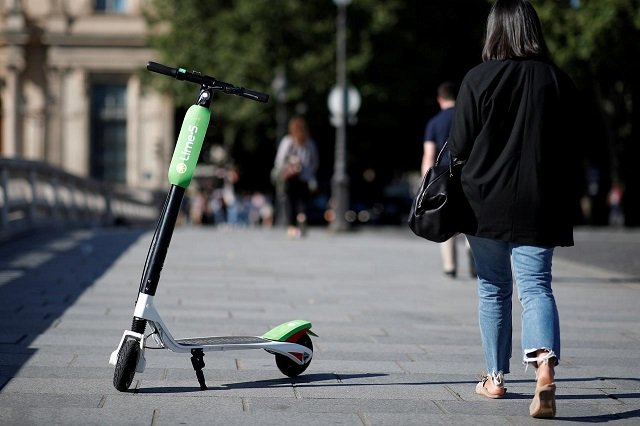 a woman walks past a dock free electric scooter lime s by california based bicycle sharing service lime displayed on their launch day in paris france june 22 2018 photo reuters