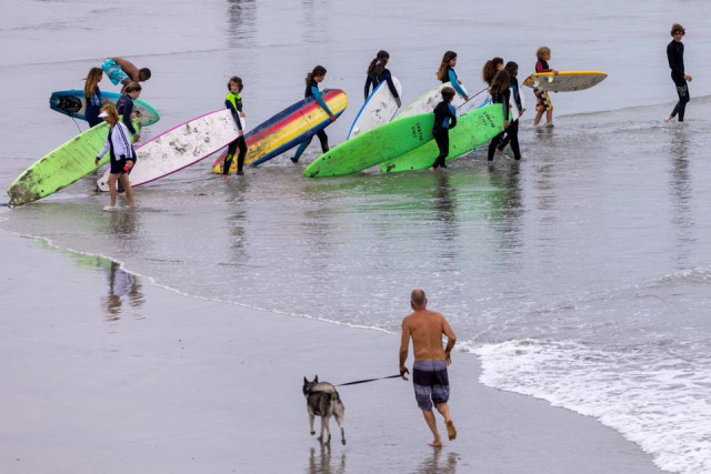a man runs with his dog as a surfing class enters the ocean during a heatwave in oceanside california us june 17 2021 photo reuters a man runs with his dog as a surfing class enters the ocean during a heatwave in oceanside california us june 17 2021 photo reuters