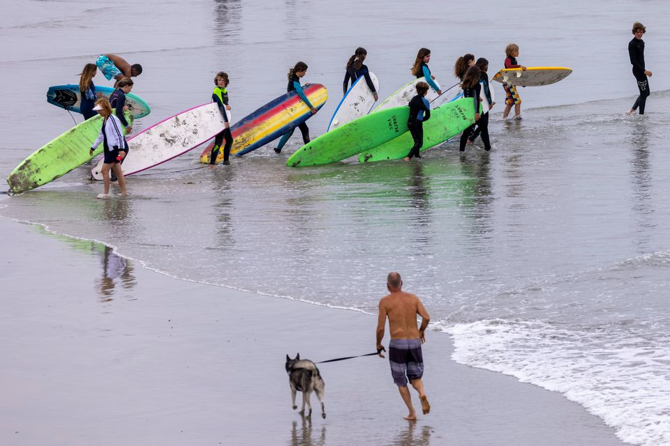 a man runs with his dog as a surfing class enters the ocean during a heatwave in oceanside california us june 17 2021 photo reuters