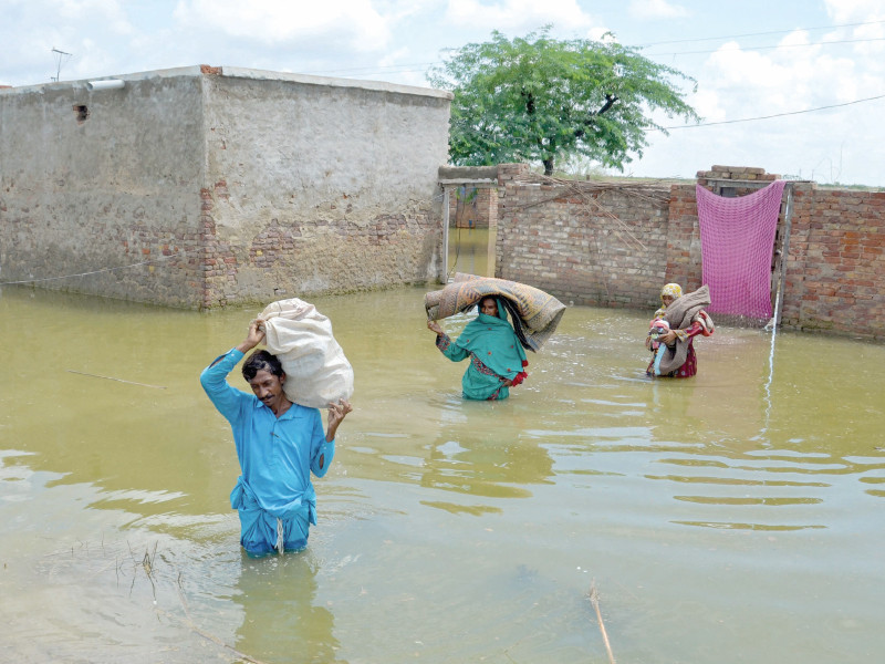 a family displaced by flood carry their belongings as they wade through floodwaters after heavy monsoon rains at sohbatpur in balochistan s jaffarabad district photo afp