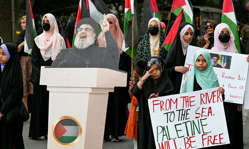 people carrying placards and palestinian national flags stand beside a portrait of slain lebanese hezbollah chief hassan nasrallah during an anti israel protest in lahore on september 28 2024 photo afp