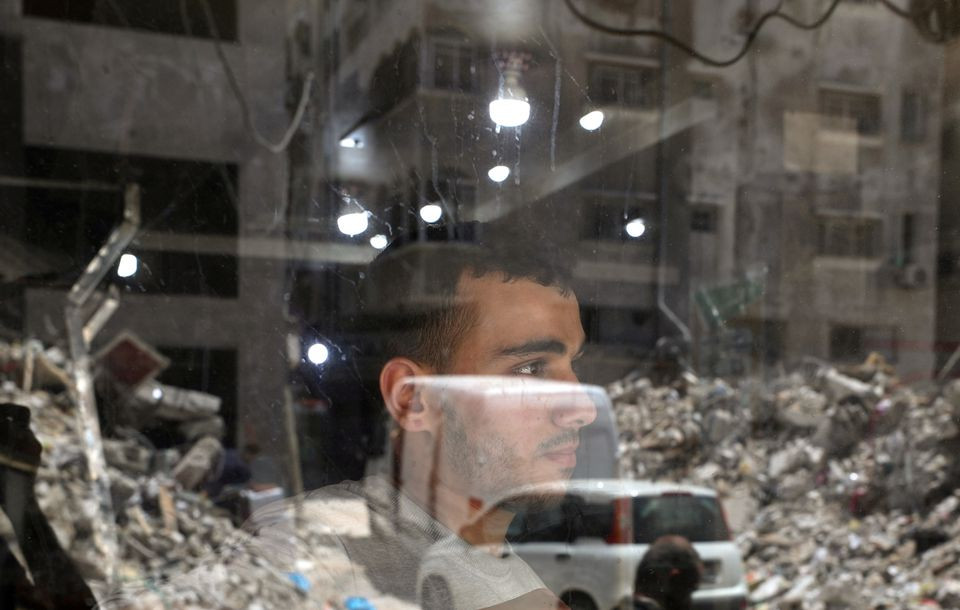 a palestinian man looks out as the remains of a building which was destroyed in israeli air strikes are reflected in a window amid israeli palestinian fighting in gaza may 20 2021 photo reuters