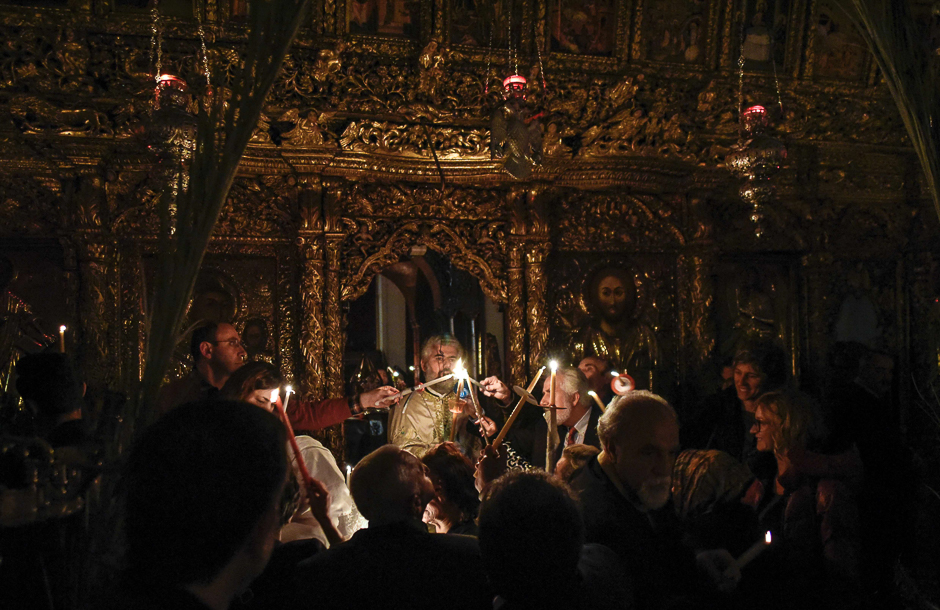 Father Venediktos Ioannou (C), Archimandrite of the Cypriot Orthodox Church of Faneromeni in the old city of Nicosia, lights up candles for other worshippers outside the altar in preparation for the Easter Saturday vigil after midnight. PHOTO: AFP