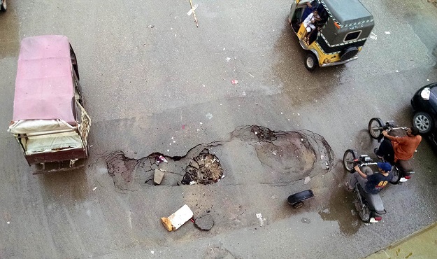 Motorists ride past the dig in the middle of a road near Nagan Chowrangi in Karachi. PHOTO: Syed Asif Ali