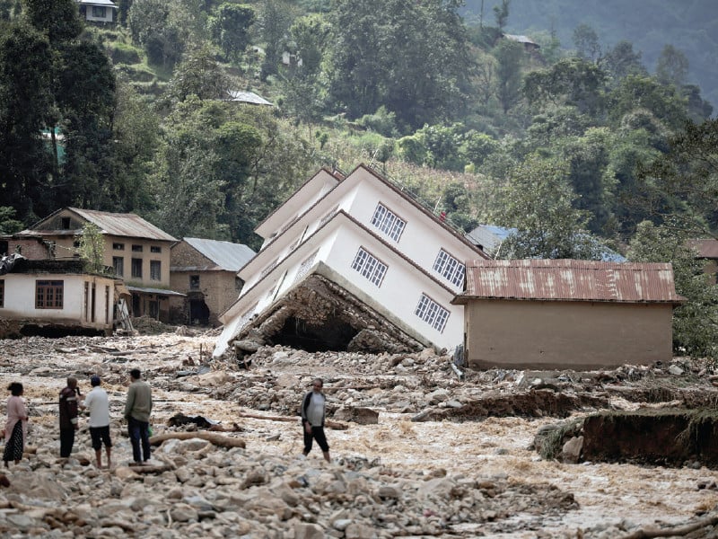 people walk along the damaged houses along the bank of roshi river at panauti in kavre nepal photo reuters