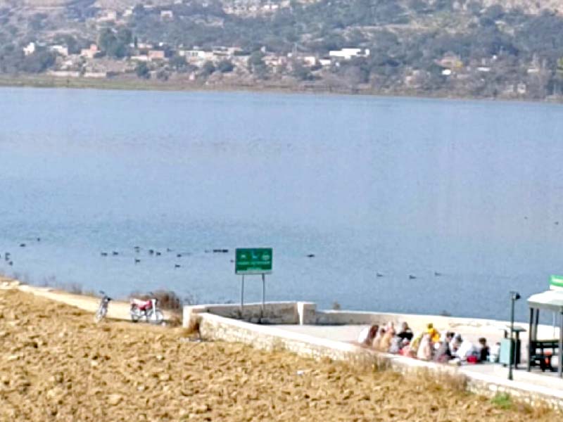 a family is sitting beside the reservoir that is located to the west of the village in soan valley photo express