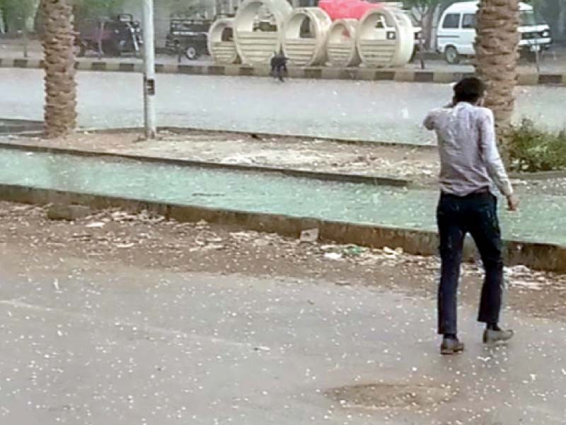 a man ducks as he crosses a road in model colony malir during a rare hailstone shower in the city on friday photo nni