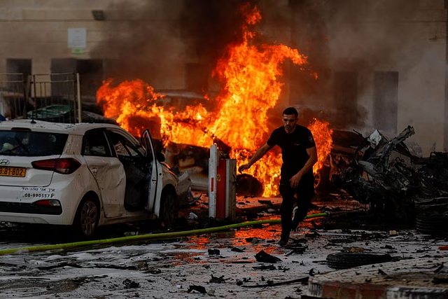 A man runs on a road as fire burns after rockets were launched from the Gaza Strip, in Ashkelon, Israel October 7, 2023. REUTERS