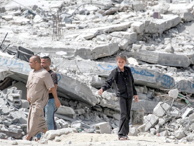 a girl and a couple of men walk past the rubble of a collapsed building in khan yunis in gaza photo afp