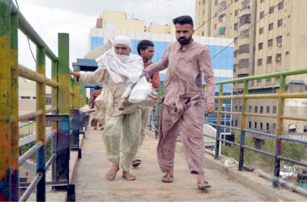 Man helps an elderly woman on a pedestrian bridge in Karachi on Tuesday. PHOTOS: EXPRESS/NNI