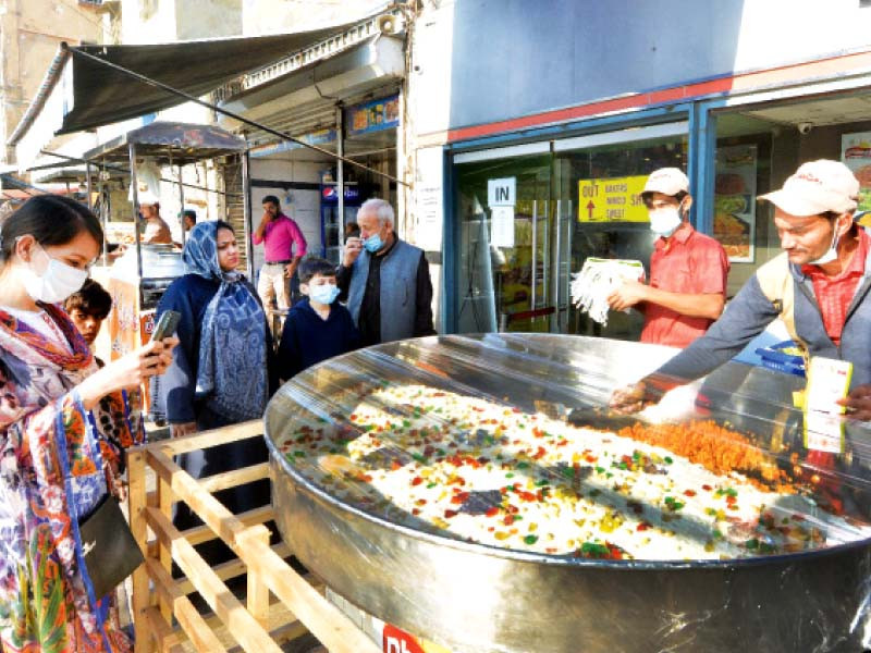 a woman takes picture of the carrot sweet dish locally called gajar ka halwa as the worker of the sweetshop packs her order at his roadside stall in karachi photo express