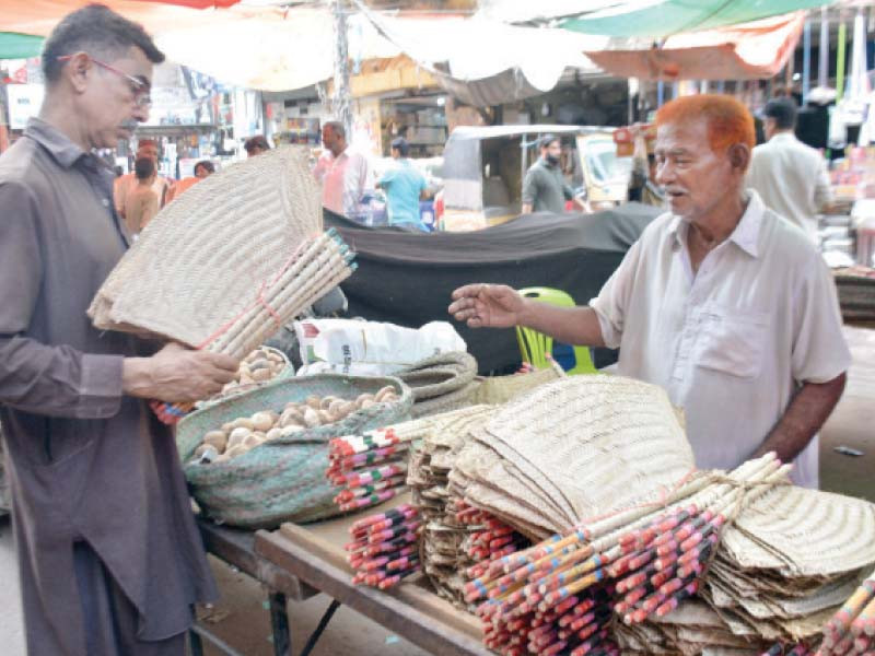 a man buys traditional fans made from date palm leaves as many areas of the city face up to 20 hour long power outages photo jalal qureshi express