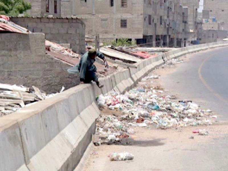 a man crosses the barrier of the lyari expressway near a slum where people have dumped garbage on the important thoroughfare photo express