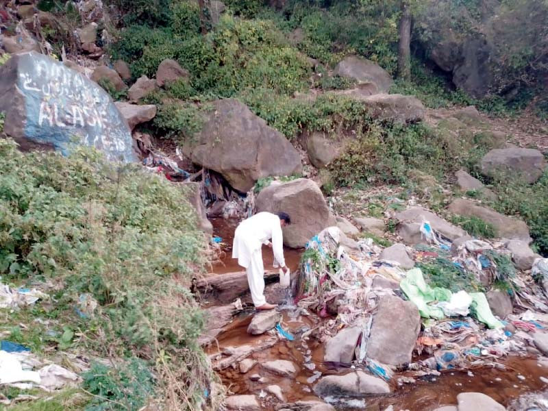 an official collects a water sample from a stream that is littered with waste photo express