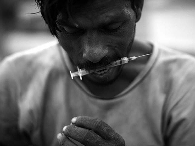 heroin addict holds a syringe between his teeth after injecting heroin in the middle of a street near kala pull karachi photo afp