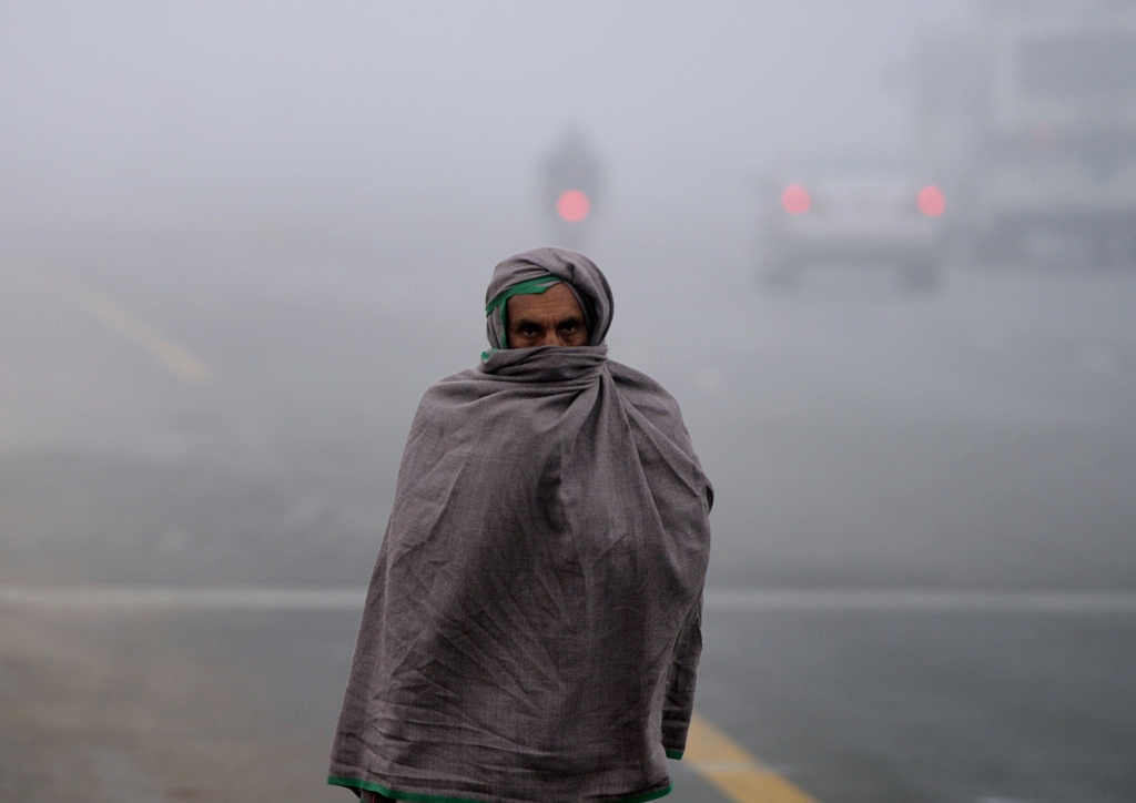 a pakistani resident covers his body with a warm shawl as he walks along a street during a cold and foggy morning in islamabad on january 8 2013 photo afp