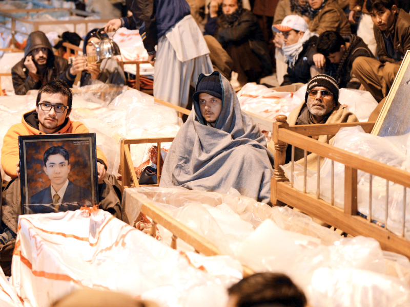 grieving relatives sit amongst the coffins and portraits of bomb blast victims in quetta on saturday photo afp