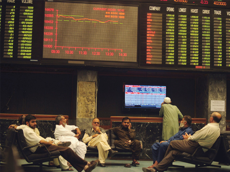 stockbrokers chat as they sit under a share price digital screen moments before the dive during yesterday s trading session at the karachi stock exchange photo afp