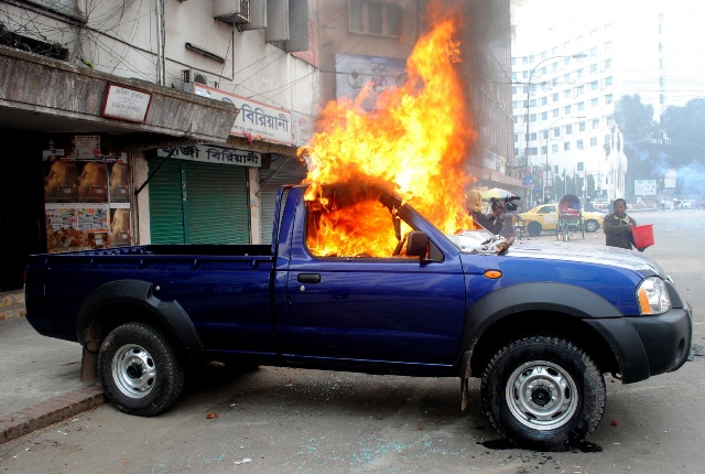 a bangladeshi bystander uses a bucket to try and put out a fire on a police car allegedly set fire to by jamaat e islami members in dhaka on january 28 2013 photo afp